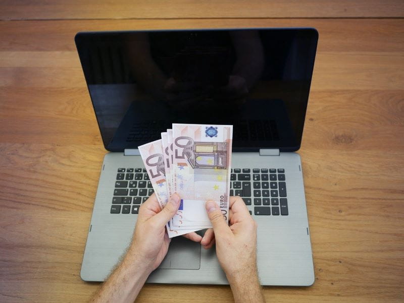 Eine Person sitzt vor dem Laptop und hält vier 50-Euro-Scheine in der Hand. 