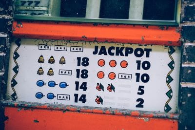 Auf einem Schild wurden zwei Walzen eines Spielautomaten nachgestellt, auf denen sich Glückssymbole und das Wort Jackpot befinden.