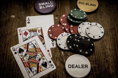 Drei Pokerkarten und mehrere Spielchips liegen auf einem Tisch.