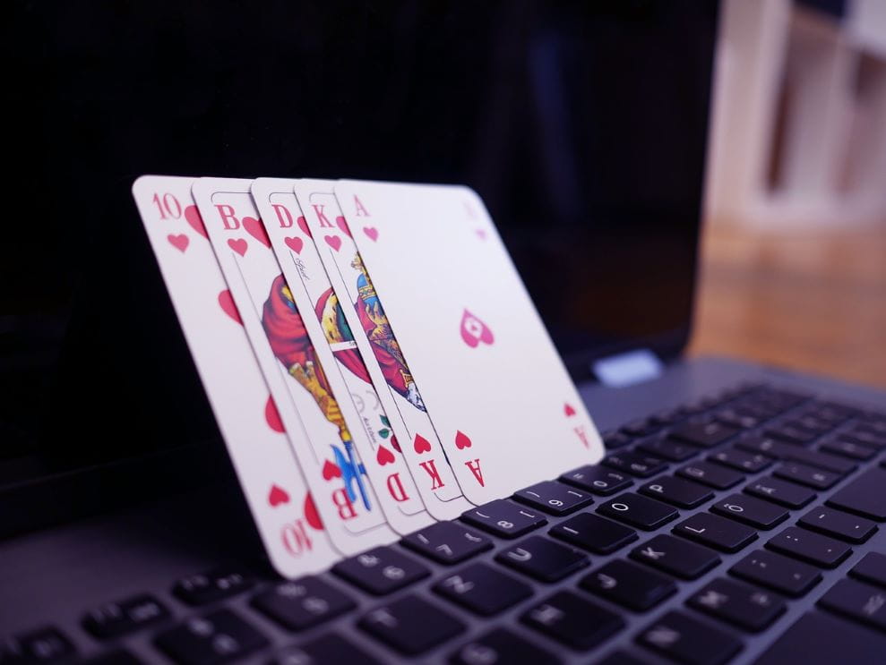 Auf einem geöffneten Laptop stehen mehrere Pokerkarten.